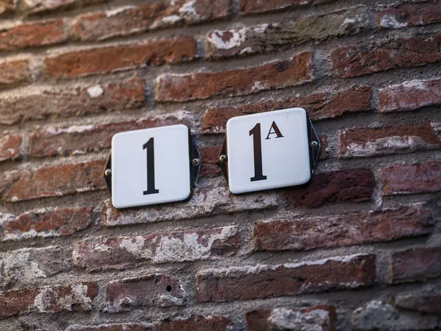 Zwei weiße Emaille-Hausnummernschilder, 1 und 1A, an einer roten Klinkerwand